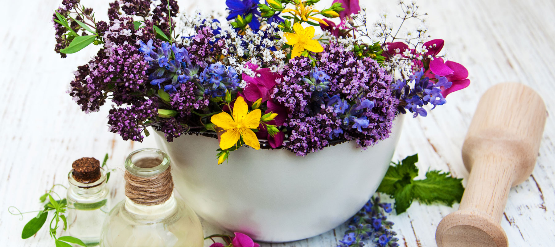 white bowl of prairie flowers with glass essential oil bottles