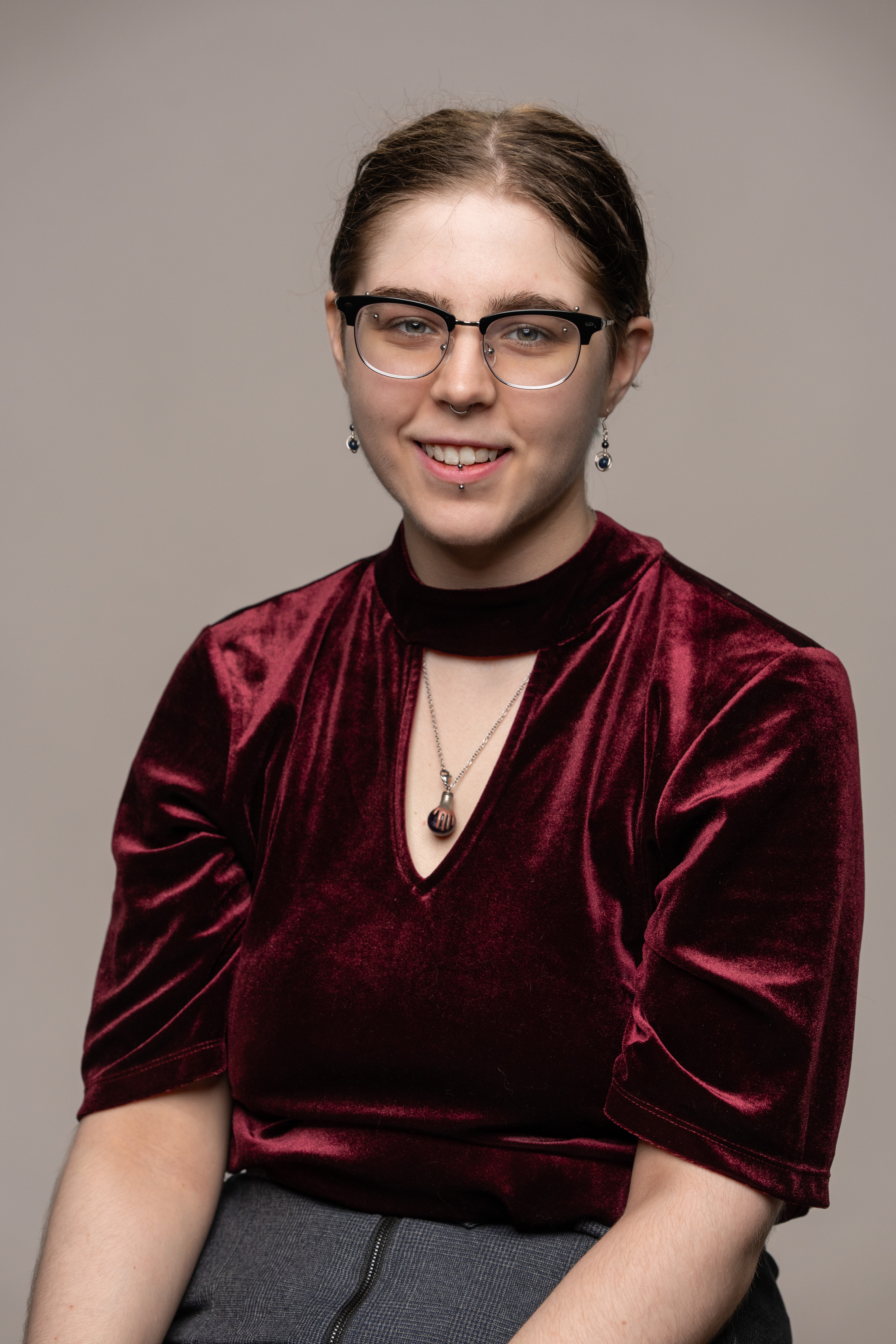Casey sitting with brown hair pulled back and wearing glasses. Red professional top and gray bottom. Casey is smiling and looking at the camera.