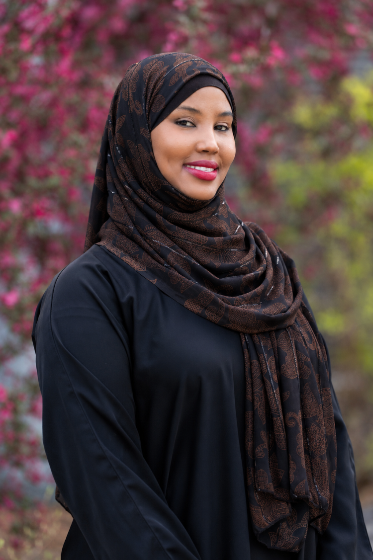 Student is looking directly at the camera and standing outside in from of blooming trees.