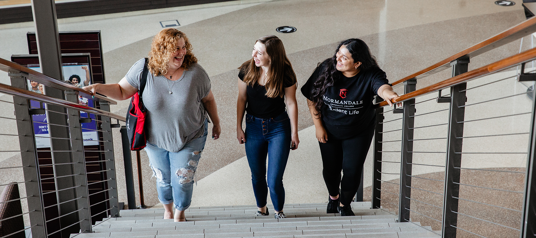 Three Normandale students walk up a staircase, talking and laughing. 