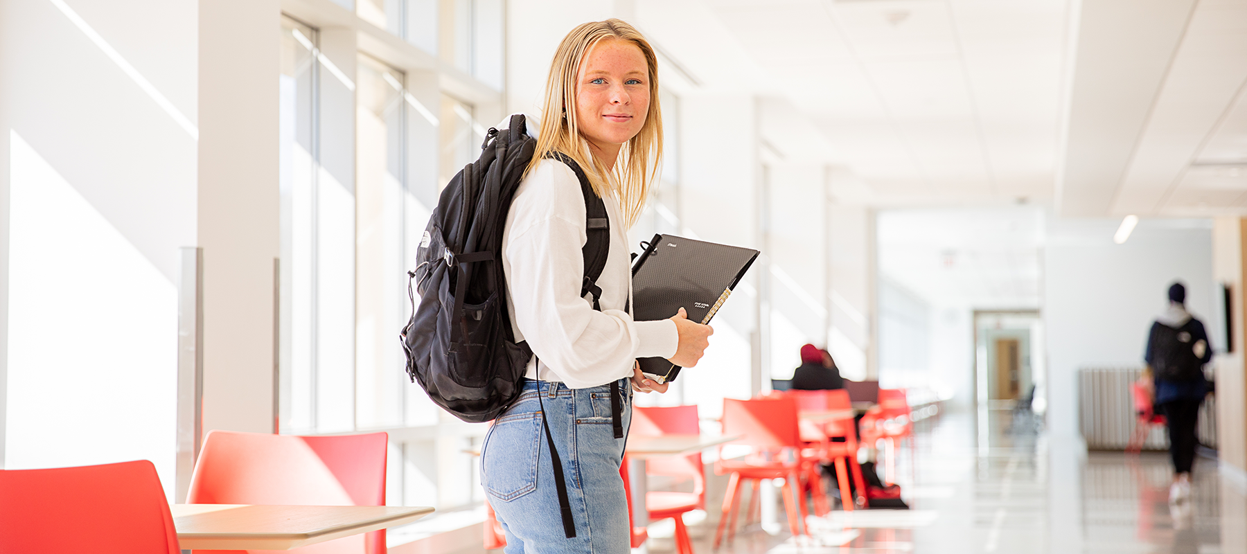 Blonde student wearing a backpack holding a laptop in a