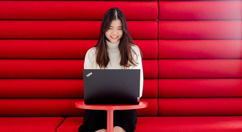  A student works at a small table with a vivid red background behind her.