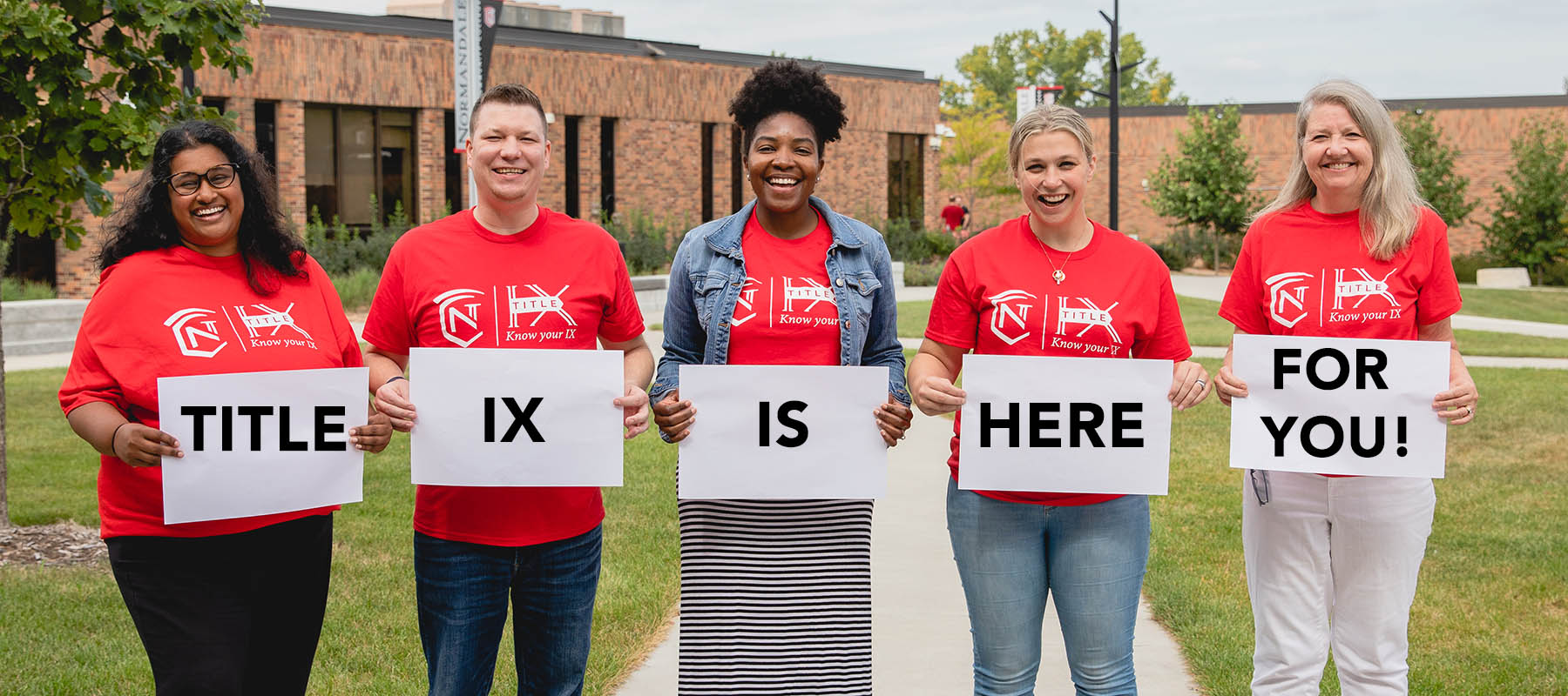 Normandale Title IX staff hold signs that say "Title IX is here for you!"