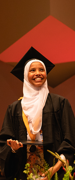 A Normandale student smiling at commencement, holding their diploma.